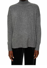 Personne portant un pull à col roulé gris côtelé à manches longues et un pantalon noir, debout les bras détendus le long du corps.