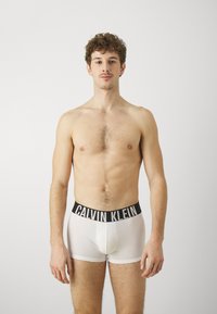 Hvite boxertruser med en svart Calvin Klein-logo på midjebåndet. Glatt, elastisk stoff med en tettsittende design som viser en minimalistisk stil.