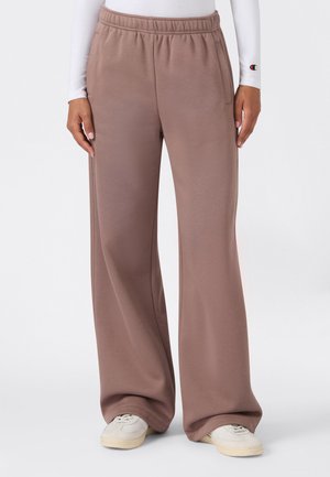 Braune weite Hose mit elastischem Bund, getragen mit weißen Sneakers und einem weißen Langarmshirt, sichtbar an Armen und Taille.