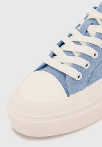 Blue canvas sneaker with white rubber toe cap and sole. Features beige laces and textured side accents, showcasing a casual design.