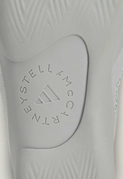 Gros plan sur une semelle intérieure grise Adidas avec le texte en relief "Stella McCartney" entourant le logo Adidas.