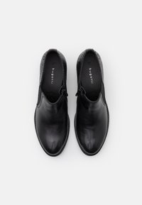 Scarpe in pelle nera con una finitura lucida e una sezione della caviglia leggermente texturizzata, dotate di punta rotonda e dettagli di cucitura minimi.