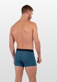 Boxers en bleu à motif avec une taille en marine, présentant un design géométrique dans des tons de bleu plus clairs. Fabriqués dans un tissu doux. Vue arrière.