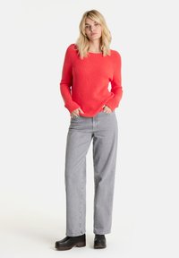 Korallenfarbener gerippter Strickpullover mit langen Ärmeln und weitem Rundhalsausschnitt, kombiniert mit hellgrauen geraden Jeans und schwarzen Plateauboots.