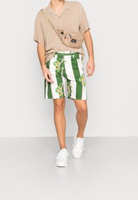 Zeleno-bílé pruhované šortky s potiskem oranžového a zeleného ovoce. Kombinovány s béžovým krátkým rukávem a bílými teniskami.