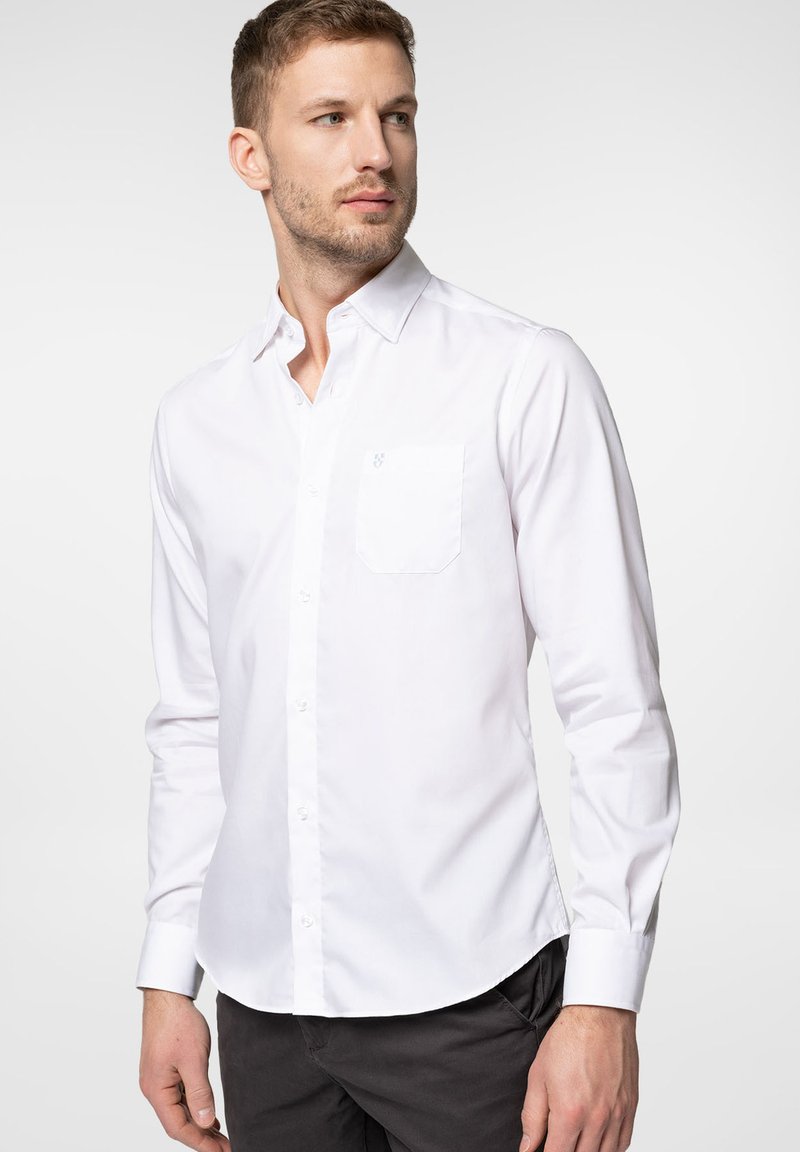 Biała koszula zapinana na guziki, wykonana z gładkiej bawełny. Posiada małą kieszonkę na lewym klatce piersiowej oraz długie rękawy z guzikami przy mankietach.
