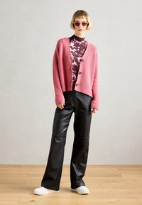 Rožinė grublėta kardiganas su mygtukais, raštuota megztinė su aukštu kaklu, juodos dirbtinės odos kelnės ir baltos platformos sportbačiai. Apvalūs saulės akiniai.