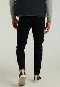 Pantalones de chándal negros con puños elásticos, detalles en el bolsillo trasero, combinados con zapatillas de deporte azul marino y un chaleco azul marino acolchado.