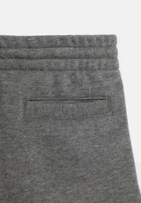Szare dresowe spodnie z teksturowanej, miękkiej tkaniny; posiadają ściągacz w pasie oraz tylną kieszeń z naszywaną klapą.