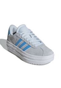 Sneaker in suede grigio con tre strisce blu, punta rotonda e una spessa suola in gomma bianca. Design con lacci e colletto imbottito.