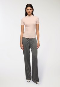 Top corto a maniche corte di un rosa chiaro con collo alla coreana abbinato a pantaloni a vita alta grigio a righe sottili e tacchi bianchi a punta. Tessuto liscio.