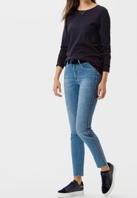 Tmavě modrá košile s dlouhým rukávem v kombinaci se světle modrými skinny džíny s kontrastním bočním pruhem. Černé tenisky doplňují celý outfit.