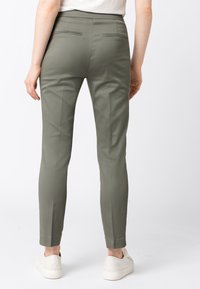 Pantaloni aderenti verde oliva in tessuto liscio, con due tasche sul retro e gambe affusolate. Abbinati a sneakers bianche.
