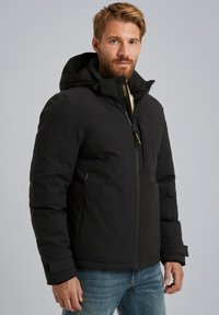 Giacca nera isolata con cappuccio, chiusura a zip anteriore e tasche laterali. Caratterizzata da una superficie liscia e polsini regolabili. Dettagli dorati sulla zip.