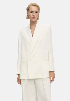 Oversized white blazer with sharp lapels, structured shoulders, and front pockets, made from a smooth, textured fabric.