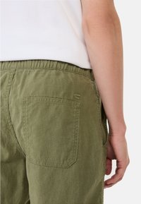 Grønne linnedshorts med elastisk talje, featuring en enkelt baglomme og en subtilt broderet brandlogo nær lomme kanten.