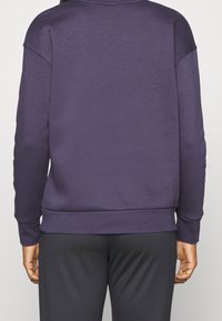 Sudadera morada de cuello redondo, con hombros caídos, puños y dobladillo de canalé, hecha de un tejido suave con una textura lisa.