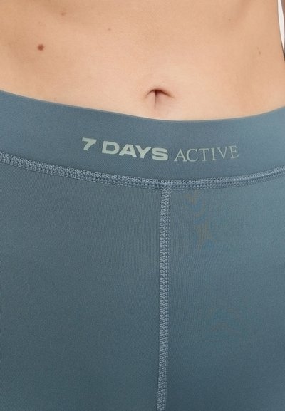 Teal športové šortky s plochým pásom s textom "7 DAYS ACTIVE" v svetlozelené farbe. Hladká textura a priliehavý strih.