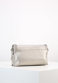 Metalická stříbrná kabelka do ruky s hladkou texturou, obdélníkovým tvarem a pletenými detaily po stranách. Uzavírá se horní klopou.