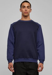 Tumesinine pusa ümarkaeluse ja raglaanvarrukatega, valmistatud tekstuurse puuvillasegust kangast. Disainis soonikkoes mansetid ja alläär, kitsas lõige.