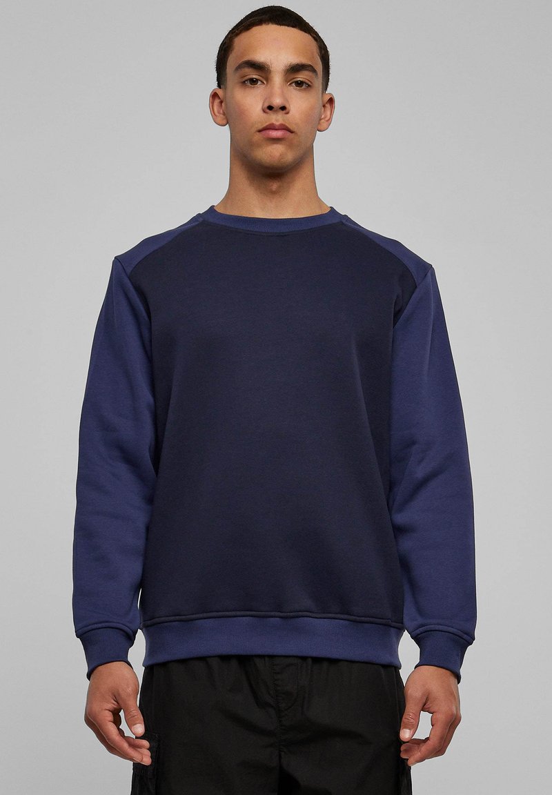 Tumesinine pusa ümarkaeluse ja raglaanvarrukatega, valmistatud tekstuurse puuvillasegust kangast. Disainis soonikkoes mansetid ja alläär, kitsas lõige.