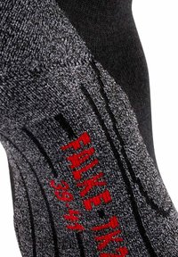 Svart och grå mönstrad strumpa med en texturerad yta, prydd med röd logotyp. Anmärkningsvärda detaljer inkluderar varierande stickmönster längs tyget.