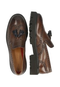 Bruna läderskor i loafermodell med broguedetaljer, tofsar och en tjock, texturerad svart gummisula. Inredningen har röd foder.