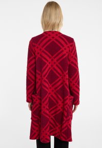 Roter langer Cardigan aus kuscheligem Stoff, mit einem auffälligen karrierten Muster in dunklerem Rot, Seitentaschen und offenem Design.