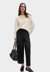 Pull côtelé crème avec encolure noire, pantalon noir ample avec ceinture, mocassins noirs brillants, porté avec un sac à main noir.