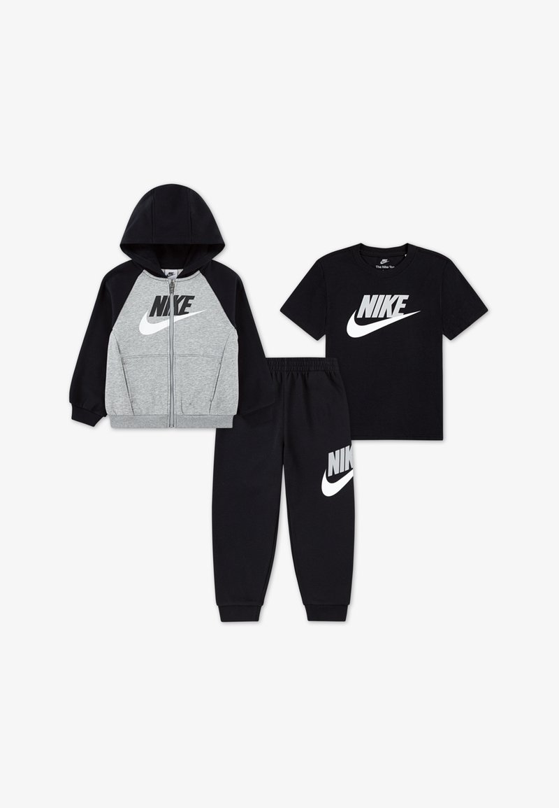 Nike drie-delige kledingset: grijze rits hoodie, zwart T-shirt met korte mouwen en zwarte trainingsbroek. Elk stuk heeft het Nike-logo prominent afgebeeld.