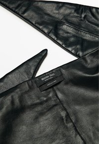 Giacca in pelle nera con texture liscia e cuciture visibili. Presenta un'etichetta con la scritta "Massimo Dutti", che indica pelle 100%.