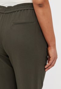 Pantalones de color verde oscuro con una textura suave, banda elástica en la cintura y un único bolsillo trasero. Diseño simple y casual sin adornos adicionales.