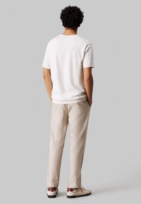 Maglione bianco a maniche corte, vestibilità comoda, abbinato a pantaloni beige e sneakers crema con accenti marroni. Design minimalista, texture morbida.