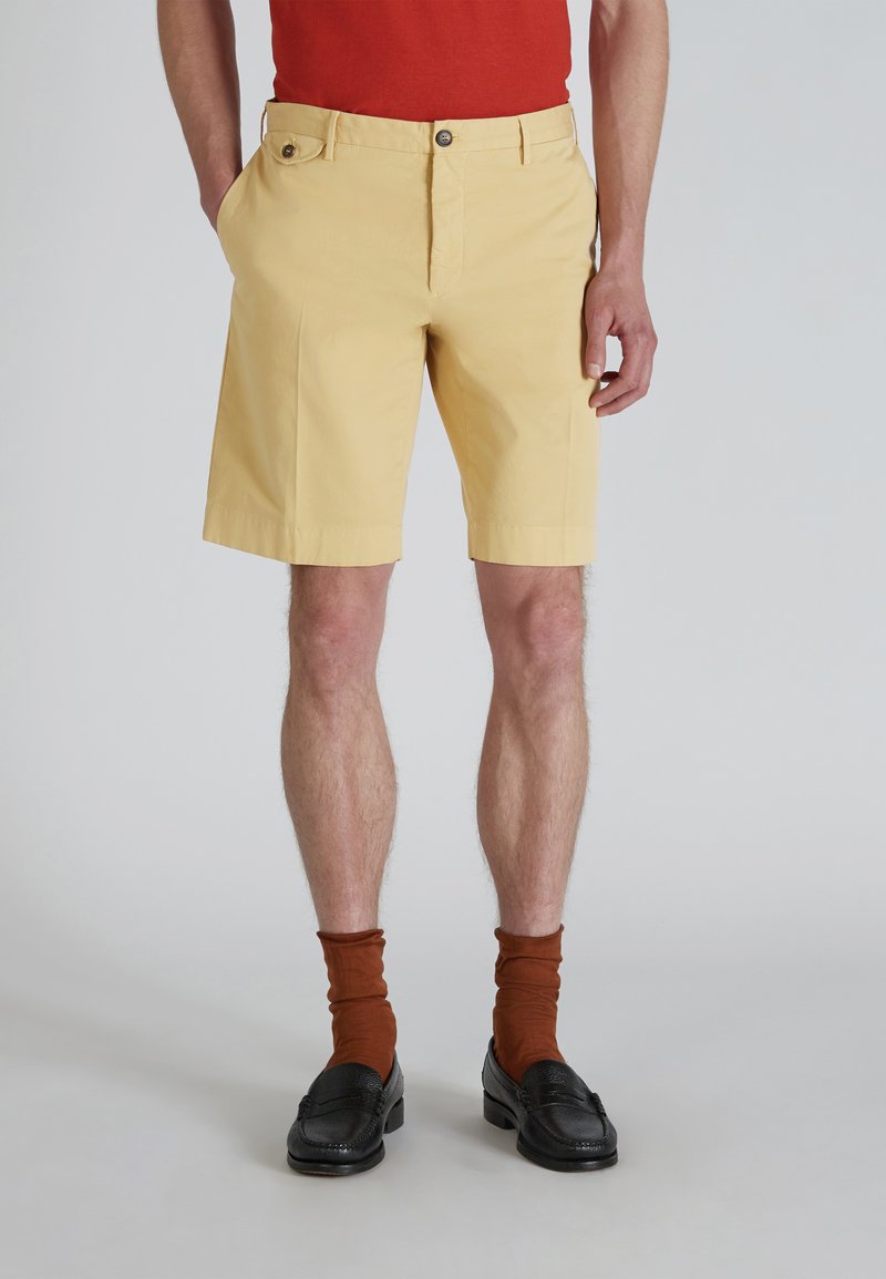 Shorts de algodón amarillos con un corte ajustado, con cierre de botón delantero y bolsillos laterales, combinados con calcetas marrones y mocasines negros.