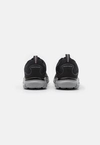 Black athletic shoes with a textured mesh upper, reflective accents, and a lightweight gray sole. Features a pull tab at the heel.