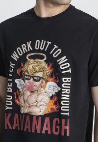 Černé bavlněné tričko s pestrou grafikou cheruba s andělským aureolem, který nosí sluneční brýle, obklopený plameny a textem.