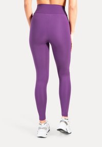 Paars legging met hoge taille gemaakt van rekbaar materiaal, met een gladde textuur en een aansluitend ontwerp, gecombineerd met witte sneakers.