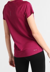 Camiseta deportiva de manga corta color granate Dri-FIT con acabado texturizado, con dobladillo redondeado y detalles reflectantes en la parte trasera.