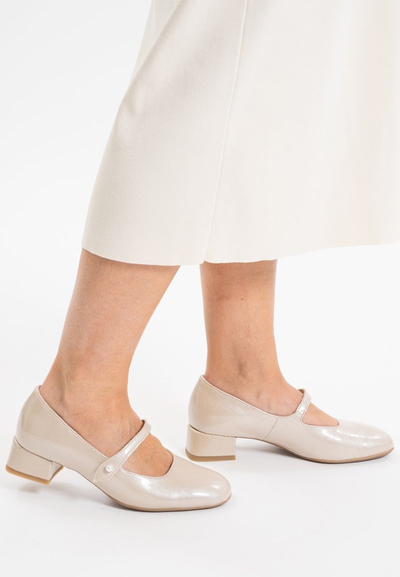 Zapatos Mary Jane en color beige con un acabado brillante, punta redondeada, una tira con un detalle de botón y un tacón bajo, estilo bloque.
