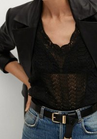 Mustassa pitsitopissa on V-pääntie, ja se on kerroksittain mustan nahkatakin alla. Asusteena on korkeavyötäröiset farkut ja musta vyö kultaisella soljella.