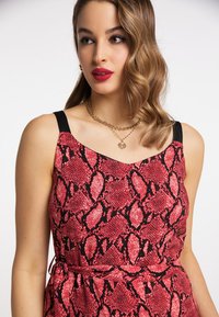 Robe en imprimé serpent rouge et noir avec de fines bretelles noires, un décolleté en V et une ceinture à la taille. Tissu lisse avec une finition brillante.