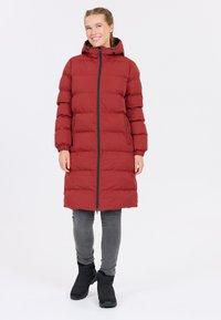 Rød pufferjakke med hætte, lange ærmer og lynlås foran. Har en quilted tekstur og justerbare snore. Sammen med grå jeans og sorte støvler.
