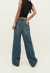 Jeans de denim de pierna ancha en azul medio, con una cintura alta, dos bolsillos traseros y un corte holgado que se estrecha en el dobladillo.