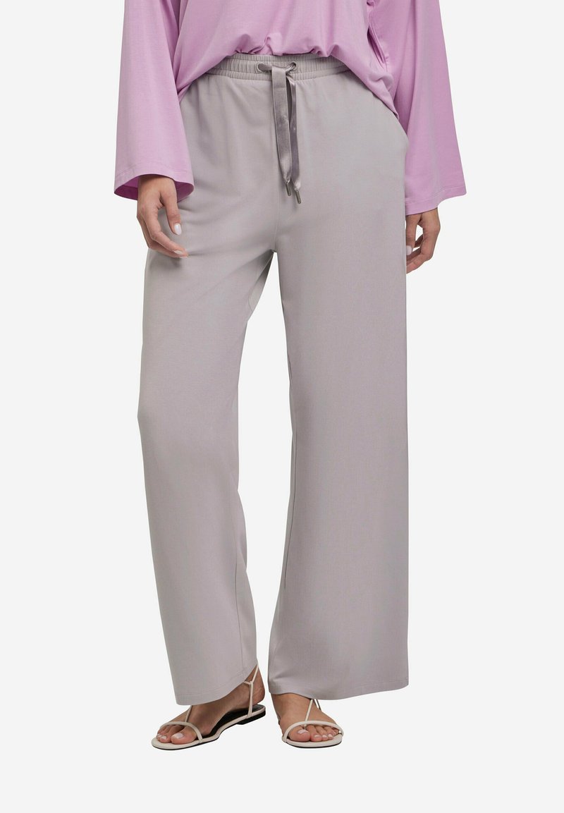 Losse, lichtgrijze broeken met een elastische tailleband, trekkoorddetail en een gladde textuur. Gecombineerd met eenvoudige, open-toe sandalen.