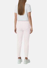 Jasnopinkowe dżinsy o dopasowanym kroju, z tylnymi kieszeniami i kontrastowym przeszyciem, w połączeniu z białym t-shirtem i szarymi trampkami.