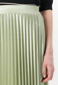Jupe plissée en satin vert clair. Présente une taille structurée avec une finition lisse et des plis verticaux sur tout le tissu.