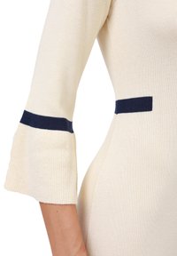 Abito in maglia color crema con una silhouette attillata. Presenta maniche a campana e accenti laterali blu navy. Texture morbida, tessuto a coste e linee pulite.