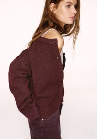 Bordó kötött kardigán bordázott mandzsettával és szegéllyel, elöl gombokkal, laza szabással, szürke trikóval és nadrággal párosítva.