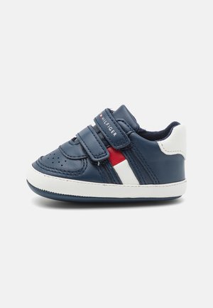 Sneaker en cuir marine avec semelle blanche, bandes Velcro et accents rouge/blanc. Présente un embout perforé et des rayures latérales contrastantes.