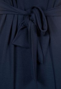 Tissu de robe bleu marine avec une texture douce, doté d'une ceinture nouée à la taille, créant des plis et des drapés dans la matière.